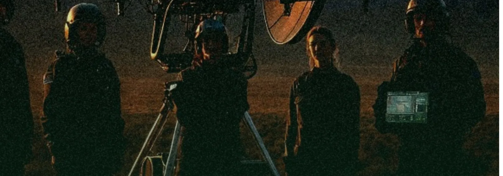 The crew at dusk in the Bear River Basin: silhouetted operators, a seeding drone and a radar dish against the last light.