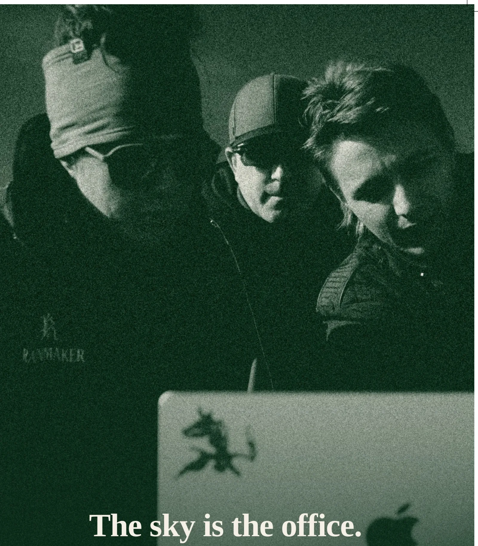 Green duotone: three crew members lean over a laptop in the dark between storm cells.